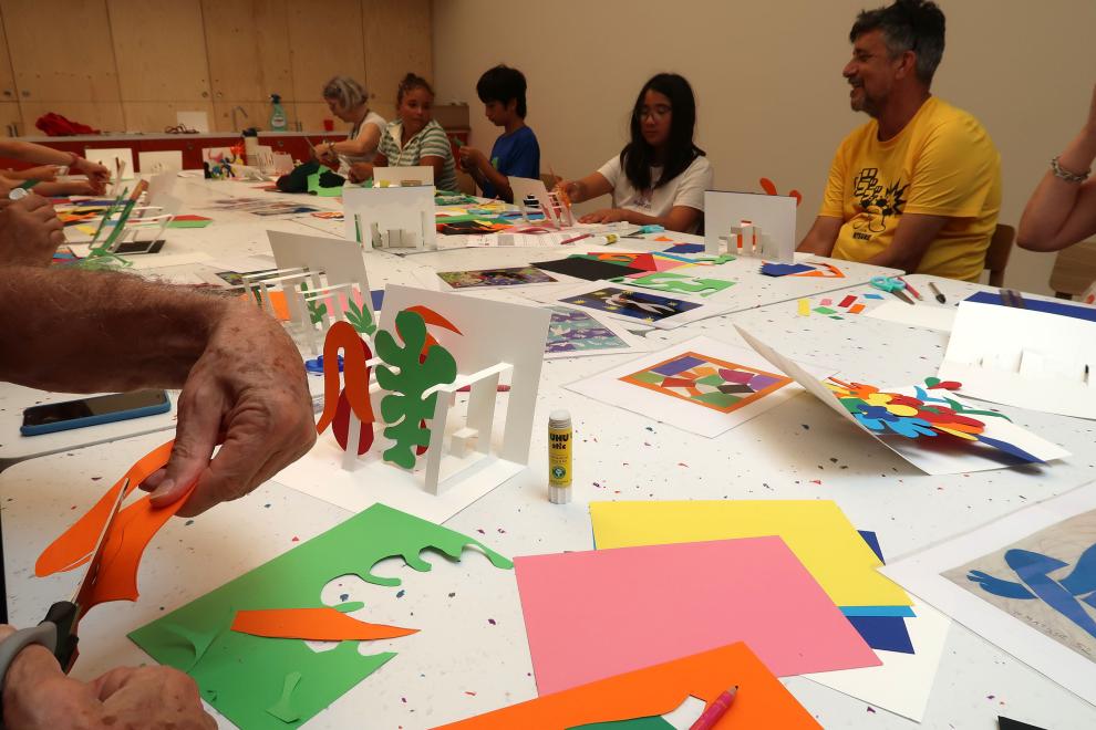 Des personnes autour d'une table découpent et assemblent des feuilles de papier colorées, lors d'une visite-atelier